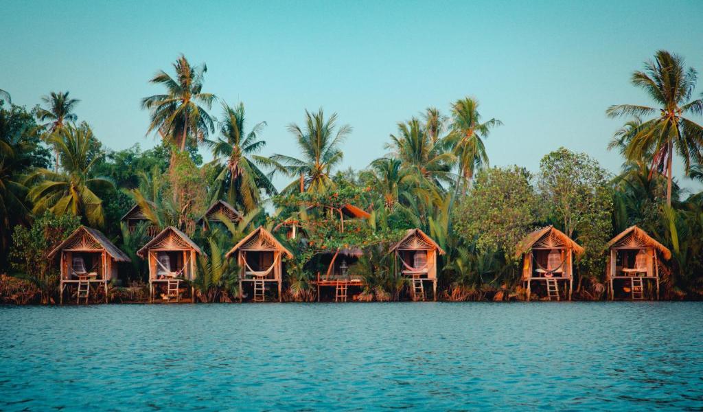 um grupo de cabanas na costa de uma massa de água em Eden Eco Village em Kampot