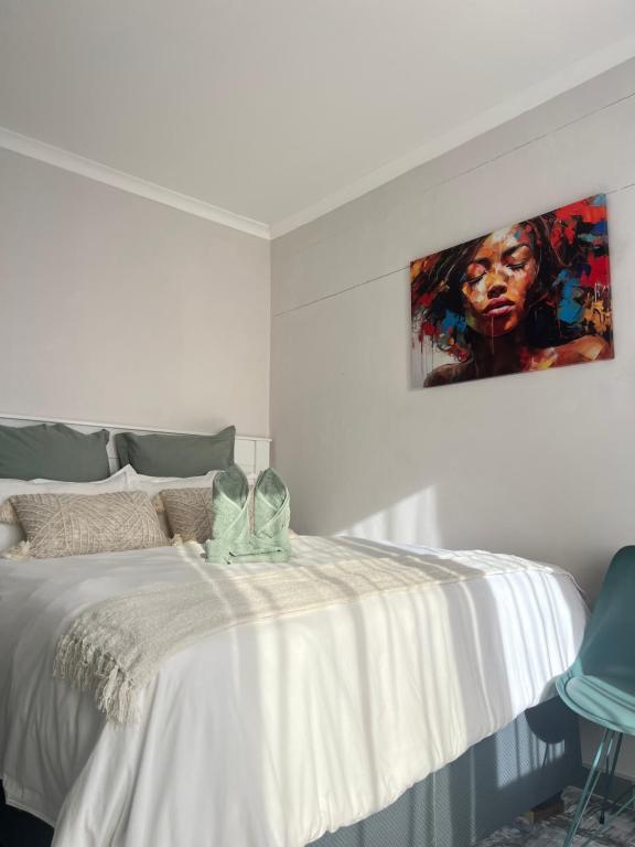 a bedroom with a white bed with a painting on the wall at Ekuku retreat in Oshakati