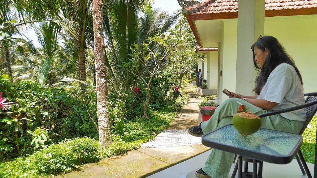 a woman sitting in a chair looking at her cell phone at Jepun Sesandan Cottage & Retreat by ABM in Selemadeg