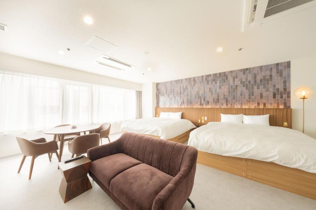 a bedroom with two beds and a couch and a table at くらしホテル Hakodate in Hakodate