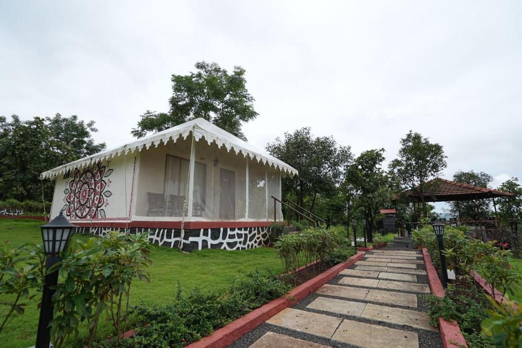 a white house with a porch and a grass yard at Gaudham Periyar Farms in Jambhulpāda