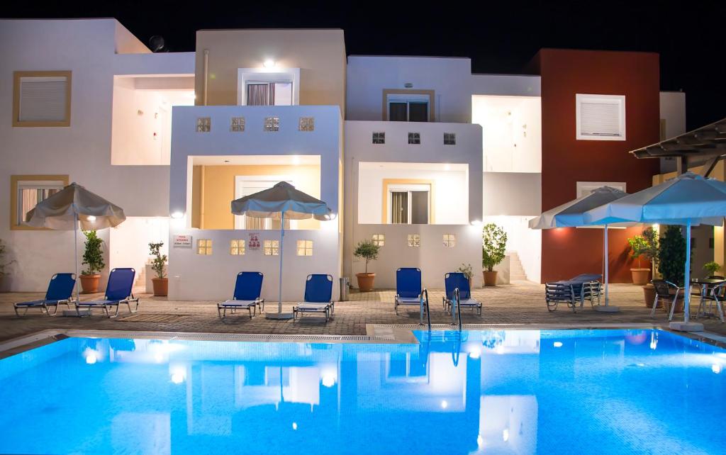 a pool with chairs and umbrellas in front of a building at Gennadi Gardens Apartments & Villas in Gennadi