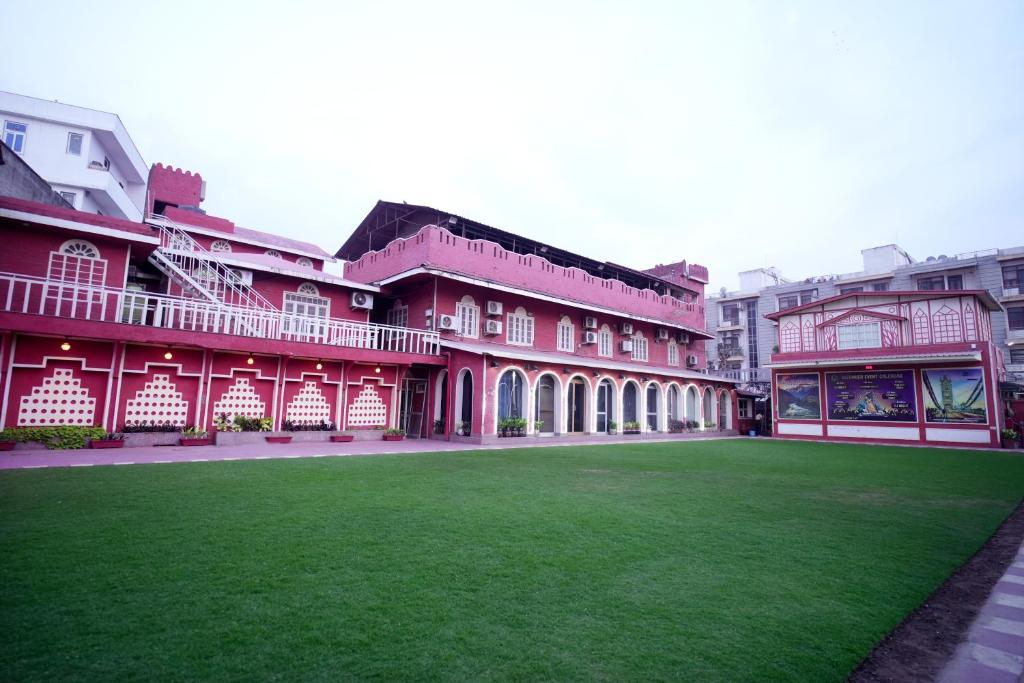 a red building with a green lawn in front of it at Canalta Hotel Restaurant Bar in Jaipur