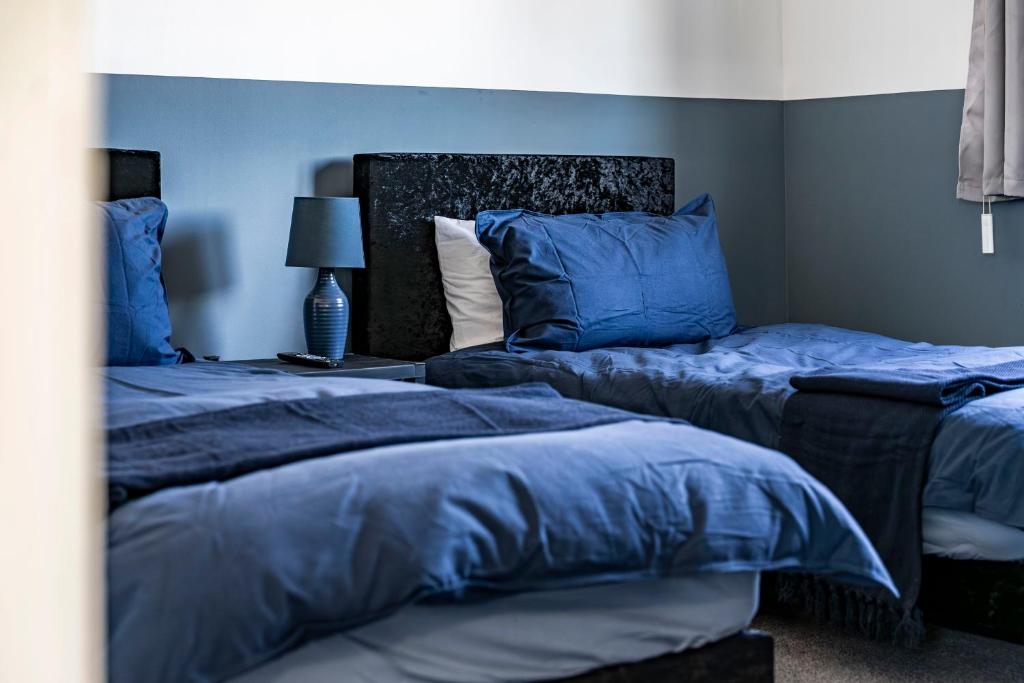 a bedroom with two beds with blue sheets and a lamp at Comfy 3 Bed House in Northampton