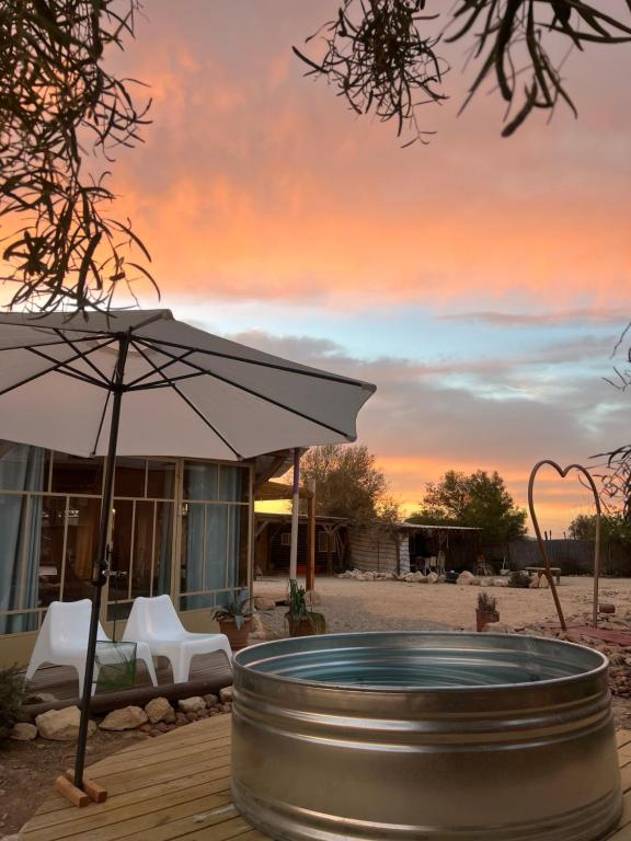 a hot tub on a deck with an umbrella at Tobiana Desert Lodging Negev in ‘Ezuz