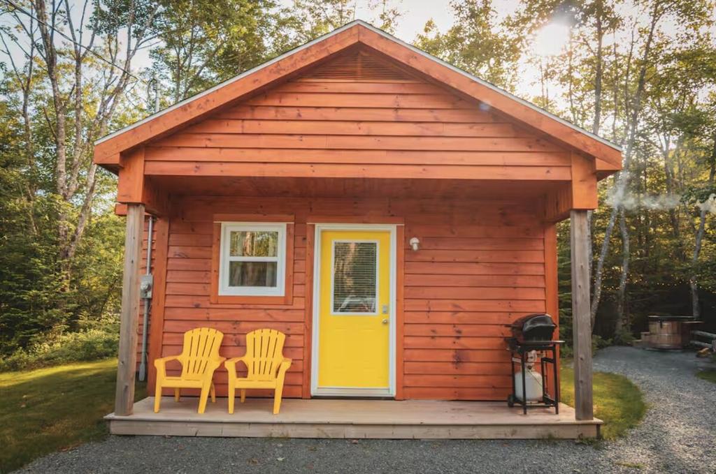 a small cabin with two chairs and a yellow door at Lawrencetown Lodge - The Maple Studio in Three Fathom Harbour