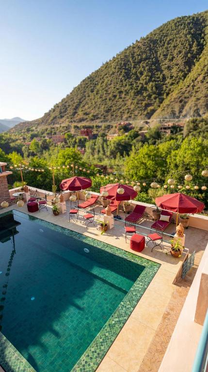 a swimming pool with red umbrellas and chairs and a mountain at villa lalla Ourika & heated pool in Aghbalou