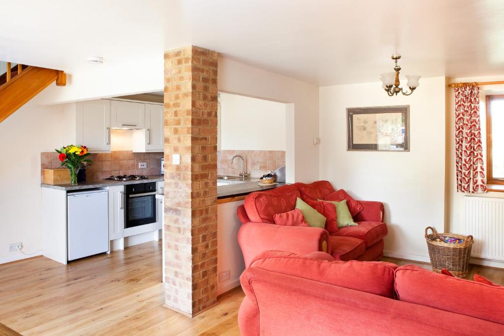 a living room with two red couches and a kitchen at Pintle Cottage in Charlbury