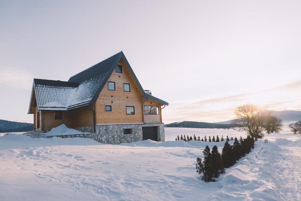 a large wooden building in a snowy field with trees at Villa Alba in Kupres