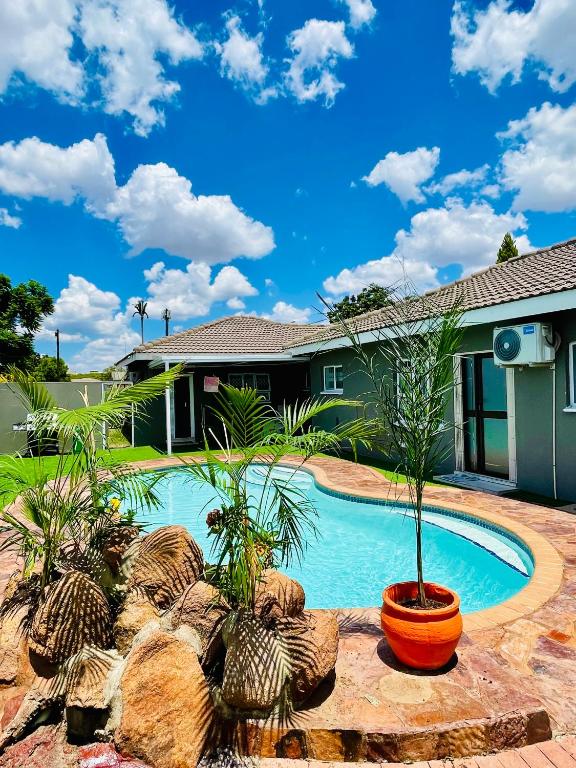 a swimming pool with palm trees and a house at Que Self Catering Apartments - Block7 in Gaborone