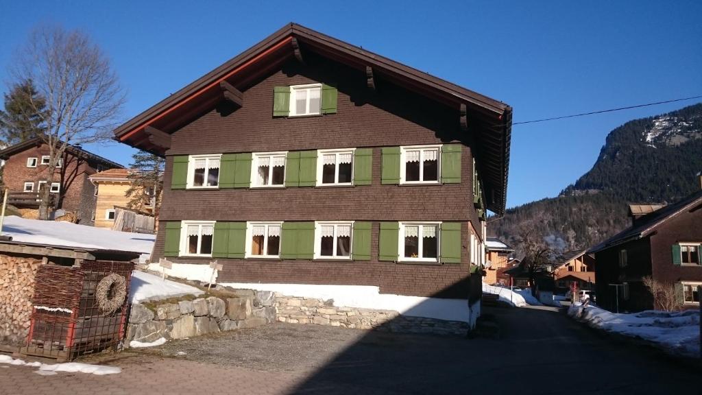 uma casa castanha e verde com neve no chão em Mein Elternhaus Gästehaus Waltraud Fink em Au im Bregenzerwald