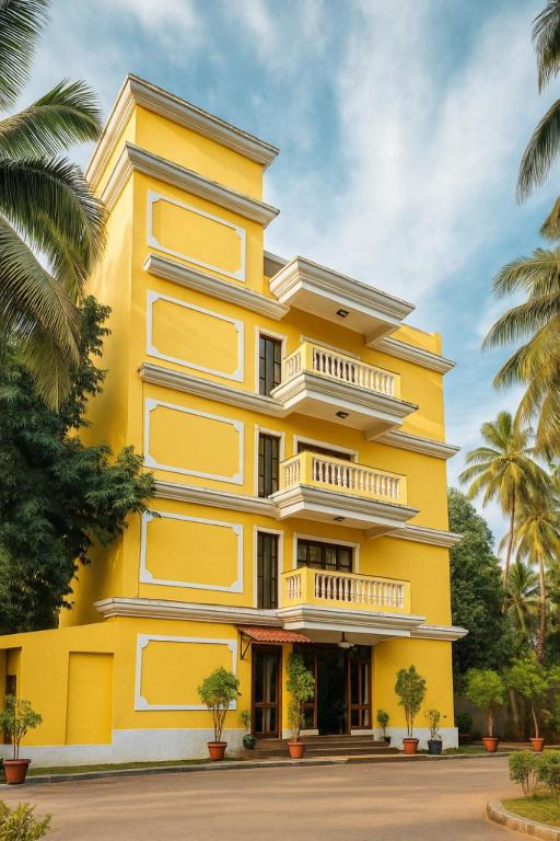 a yellow building with palm trees in front of it at Sonikas Holiday Homes (Studio) in Candolim