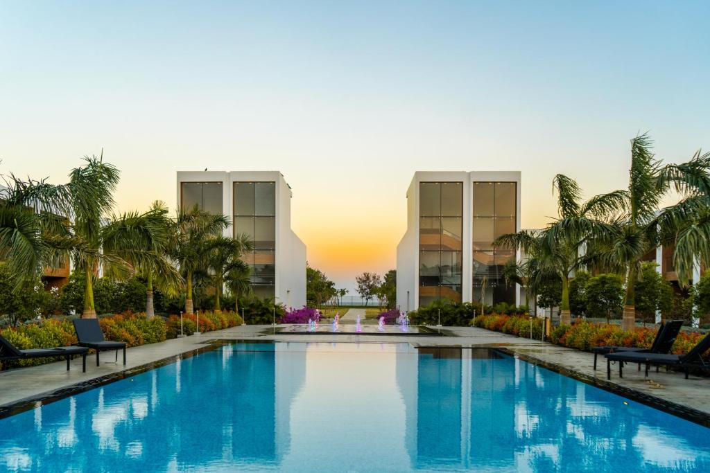 a pool in front of a building with palm trees at The Shore Trishvam in Pondicherry