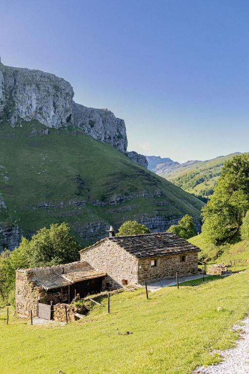 two stone buildings in a field with a mountain in the background at Cabañas con Encanto in San Roque de Ríomiera
