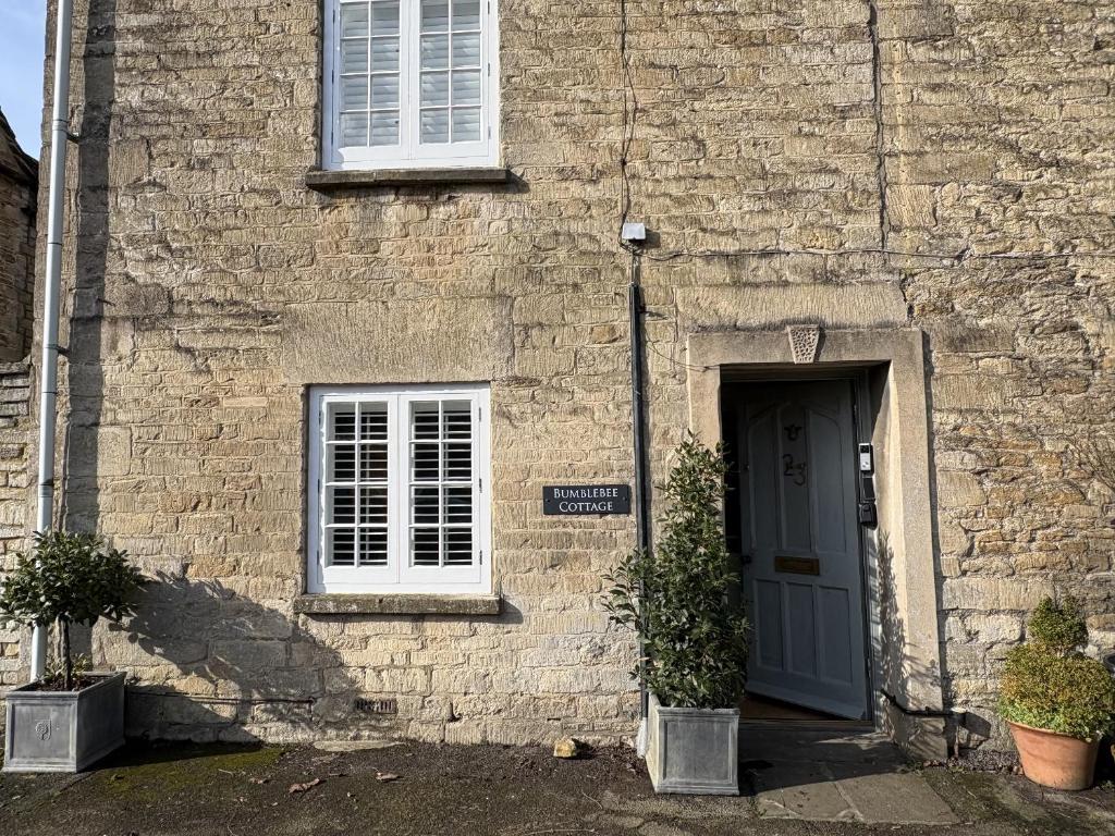 a stone building with a blue door and a window at Bumblebee Cottage in Tetbury