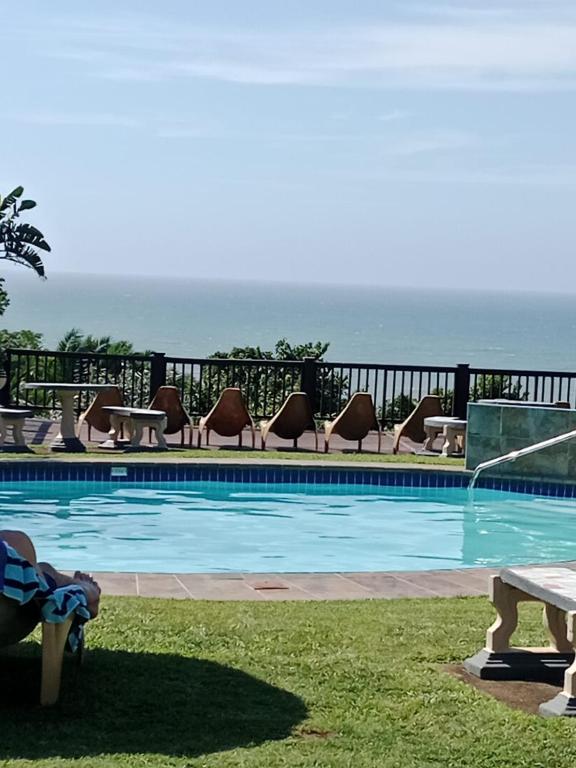a swimming pool with chairs and the ocean in the background at Umzumbe Chalets Share Block ltd in Umzumbe