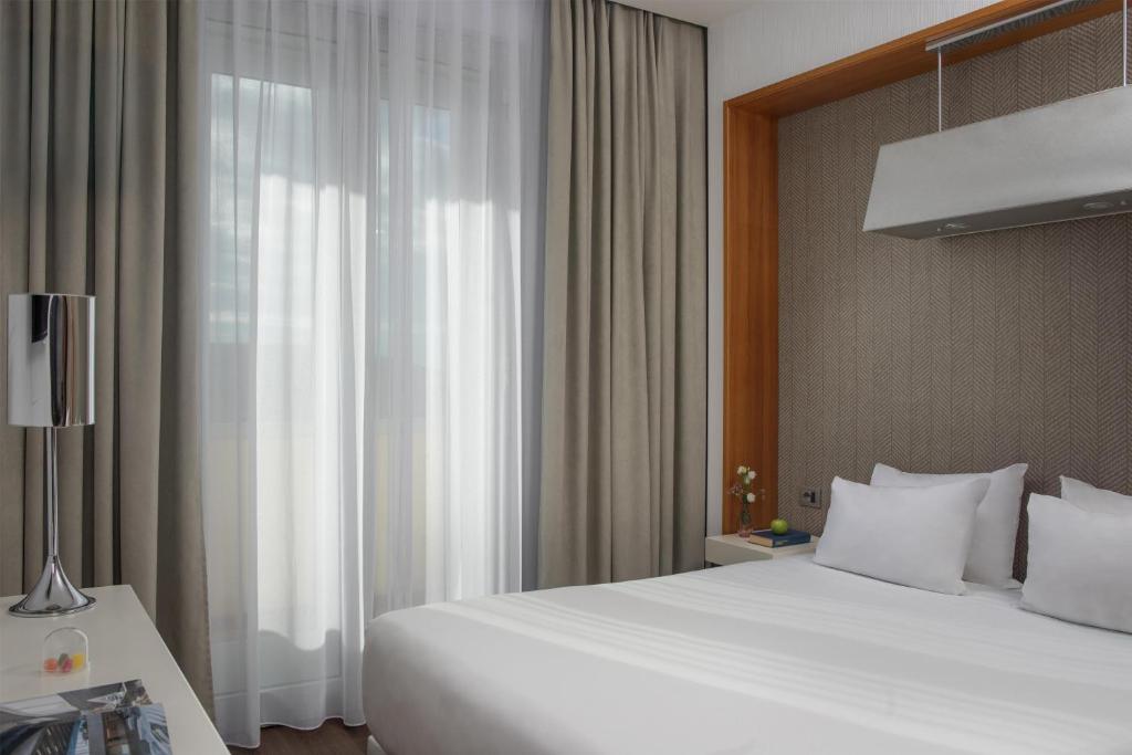 a bedroom with a large white bed and a window at NH Pisa in Pisa