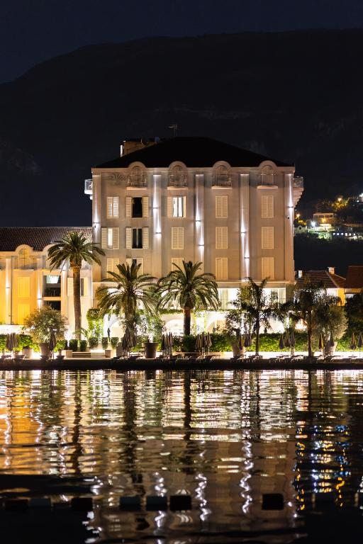 ein Gebäude mit Palmen vor einem Gewässer in der Unterkunft Hotel Palma in Tivat