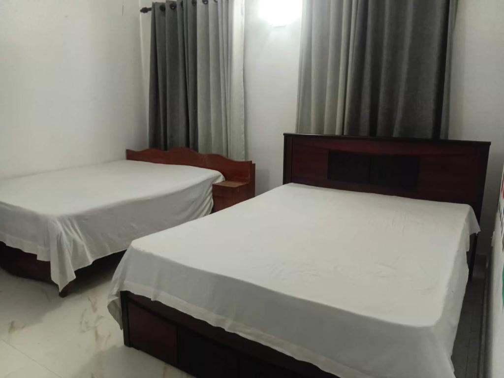 two beds in a room with white sheets at Akshi Hostel in Kandy