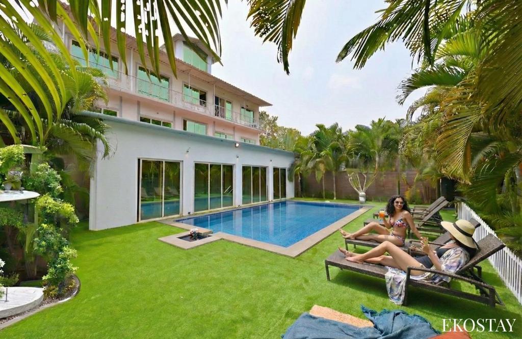 two women sitting on chairs in front of a house with a swimming pool at Ekostay - Crown Villa in Alibaug