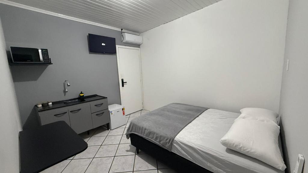 a bedroom with a bed and a sink and a microwave at Flat completo em excelente localização in Chapecó