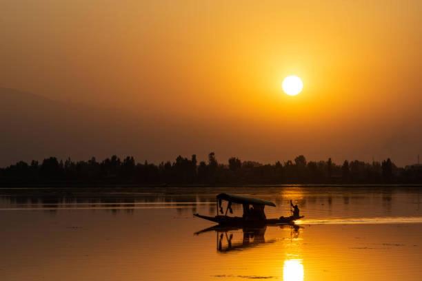 a small boat in the water with the sunset in the background at White blossom in Srinagar