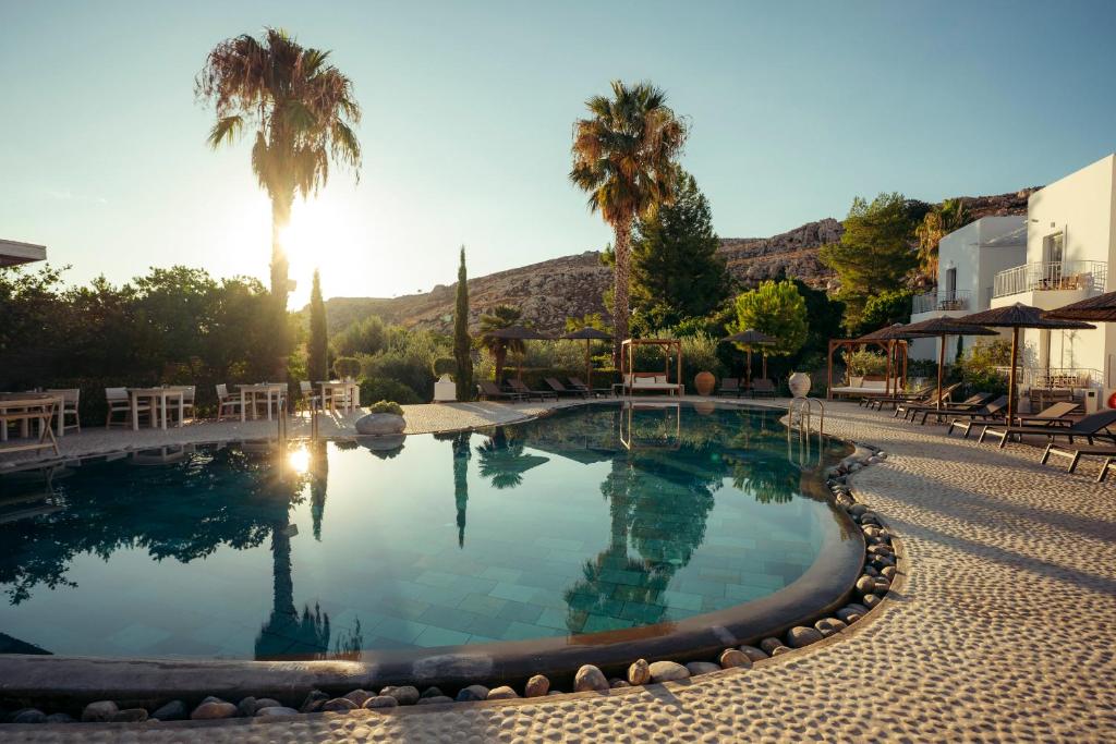 ein großer Swimmingpool mit Palmen und einem Gebäude in der Unterkunft Caesars Gardens Hotel & Spa - Adults Only in Lindos