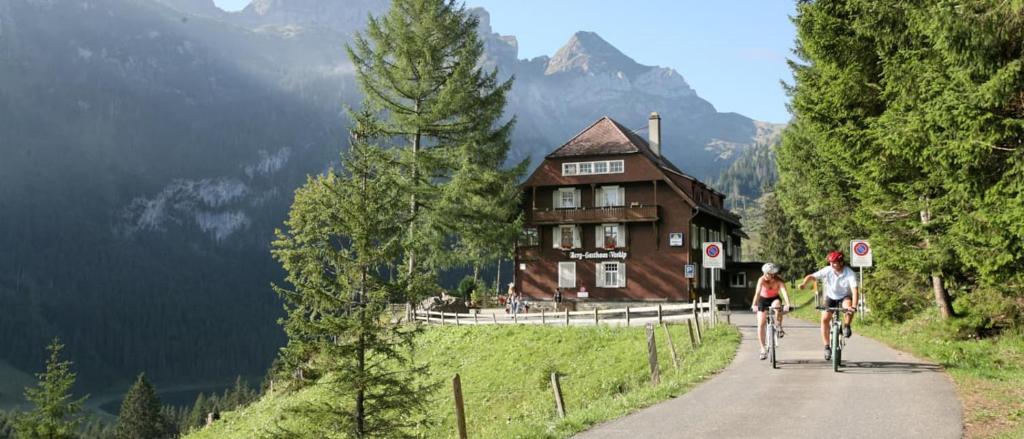 two people riding bikes down a path in front of a house at Berggasthaus Voralp in Grabs