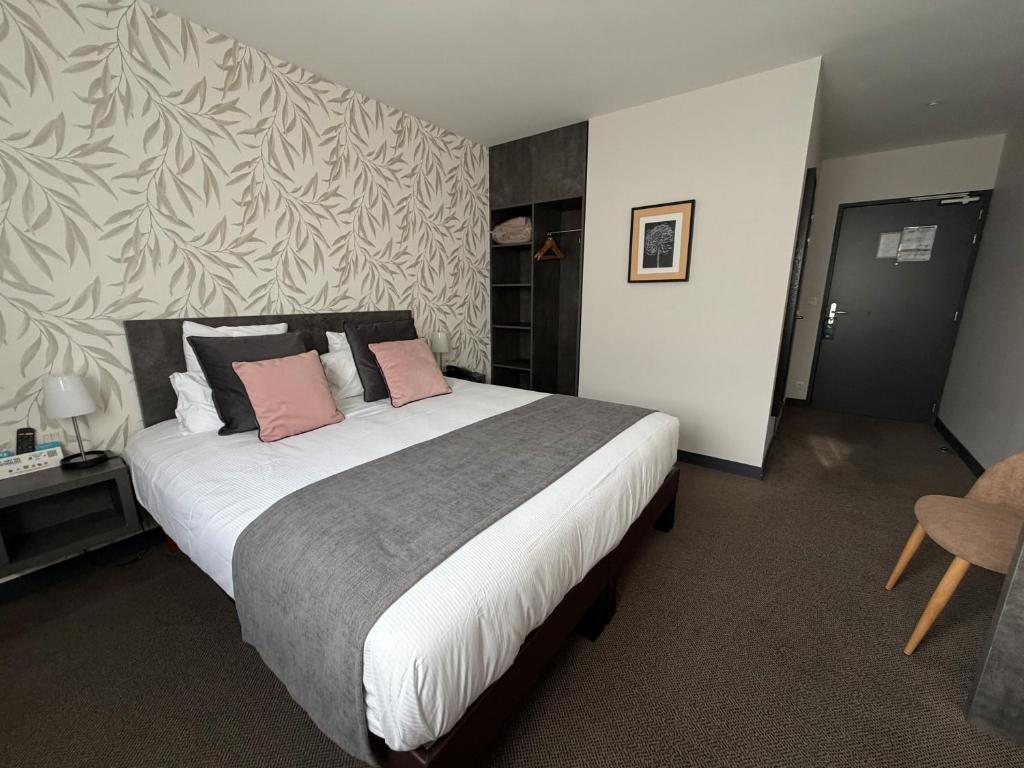 a bedroom with a large bed with two pink pillows at LOGIS Hôtel ARCADIA in Lannion