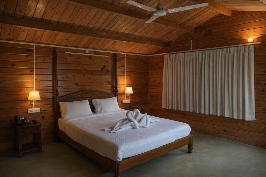 a bedroom with a bed with white sheets and wooden walls at B R Cottages, 200 meters from Patnem Beach in Canacona