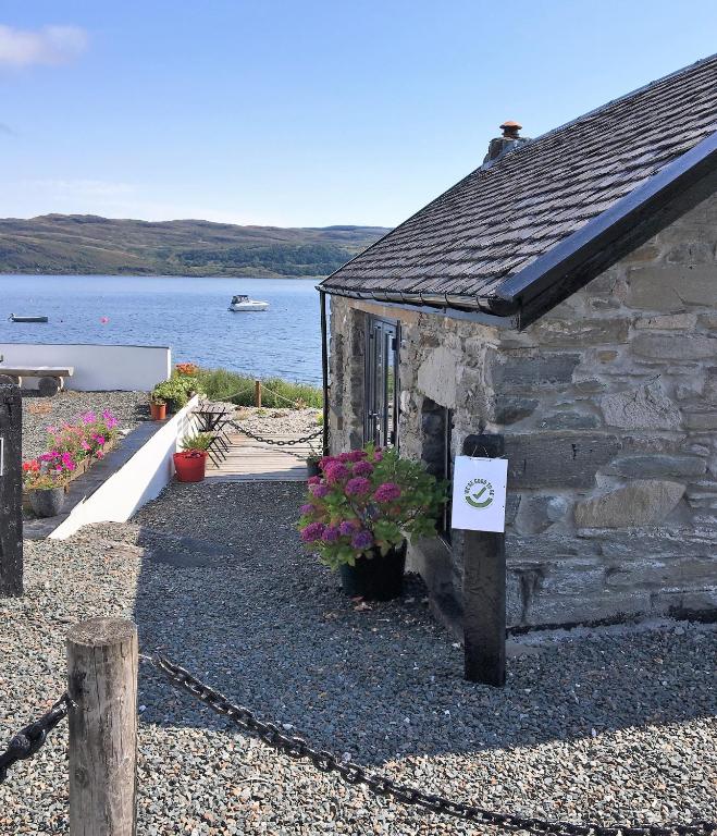 a stone building with a sign on it next to the water at Pier Cottage at Kames in Kames