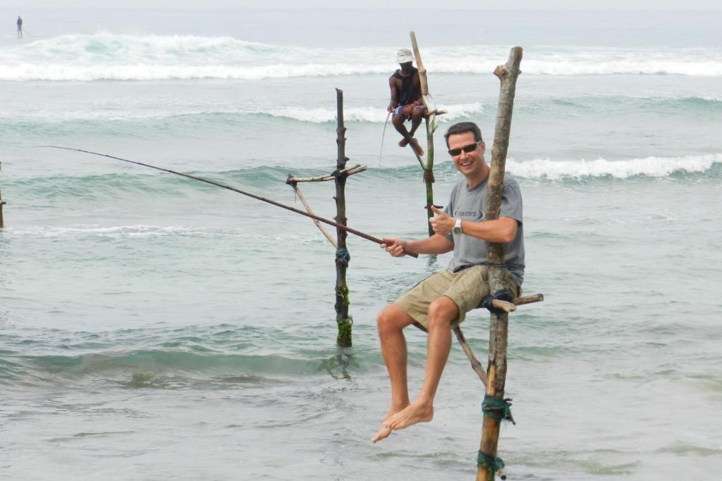 a man is sitting on a pole in the ocean at Dilco Villa Ahangama in Ahangama