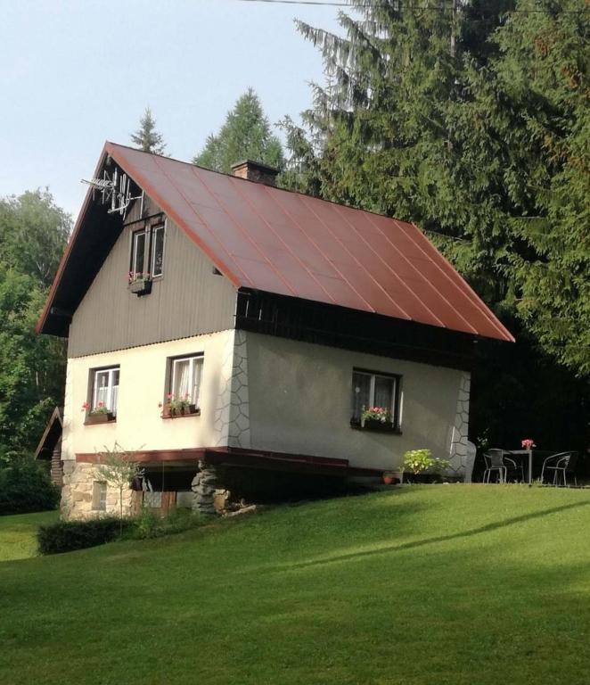 a house with a red roof on a green lawn at Chata v Poustce in Benecko