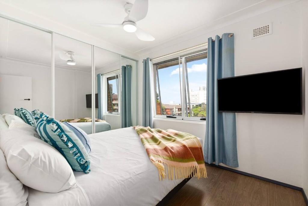 a bedroom with a white bed and a flat screen tv at Shoreleaf Haven - Moments from Waves & Seaside Eats in Deewhy