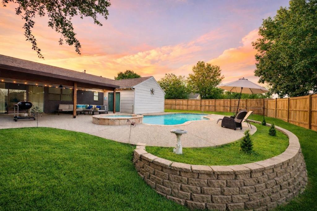 a backyard with a swimming pool and a stone wall at DFW Retreat - Pool, Spa & Minutes to Dallas & Fort Worth in Flower Mound