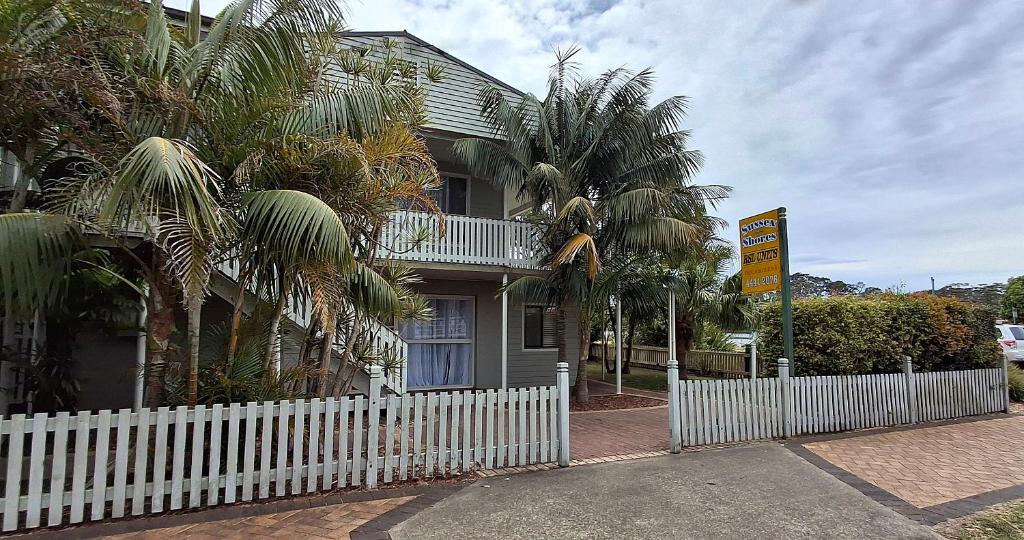 a white fence in front of a house with palm trees at Sussex Shores in Sussex Inlet