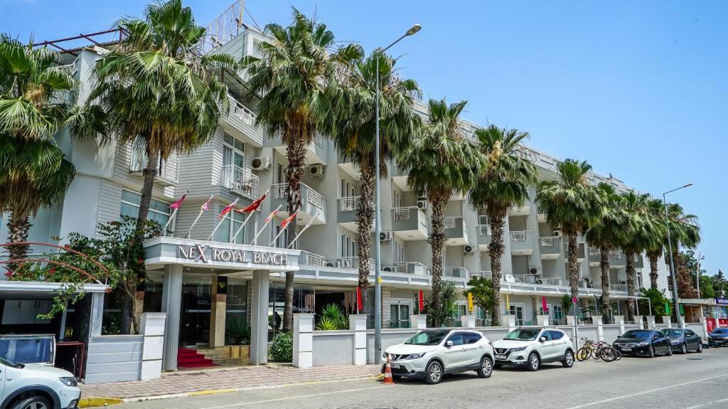 a large white building with palm trees in front of it at Nex Royal Beach in Antalya