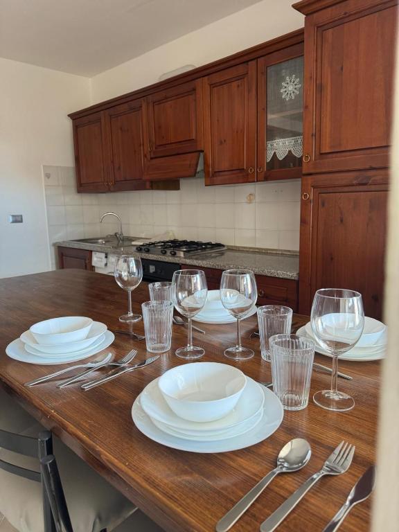 a wooden table with plates and wine glasses on it at Appartamento Trieste Airport in Ronchi dei Legionari