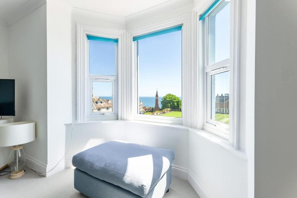 a white room with windows and a blue ottoman at Rooftop Hideaway -Central Coastal Flat - Sea Views in Seaton