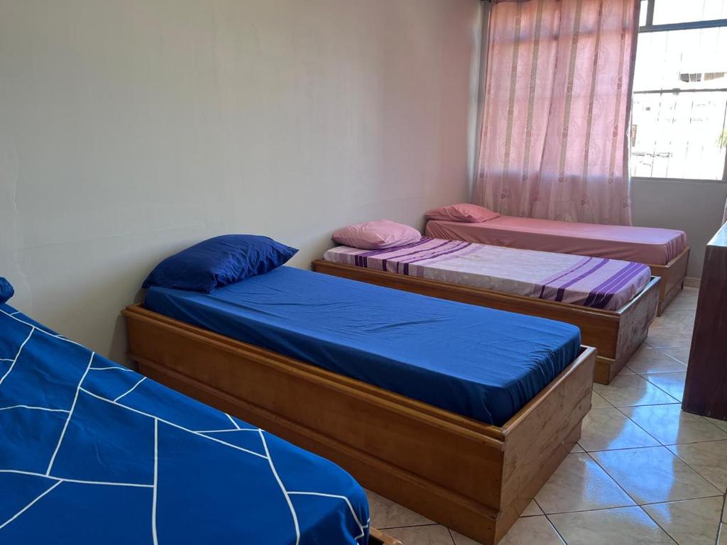 three beds in a room with blue and purple sheets at Pousada Fronteira City in Foz do Iguaçu