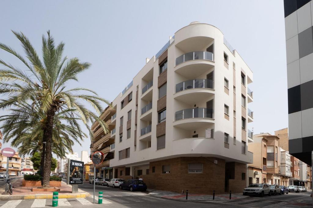a tall white building with a palm tree in front of it at He Musica in Torrevieja