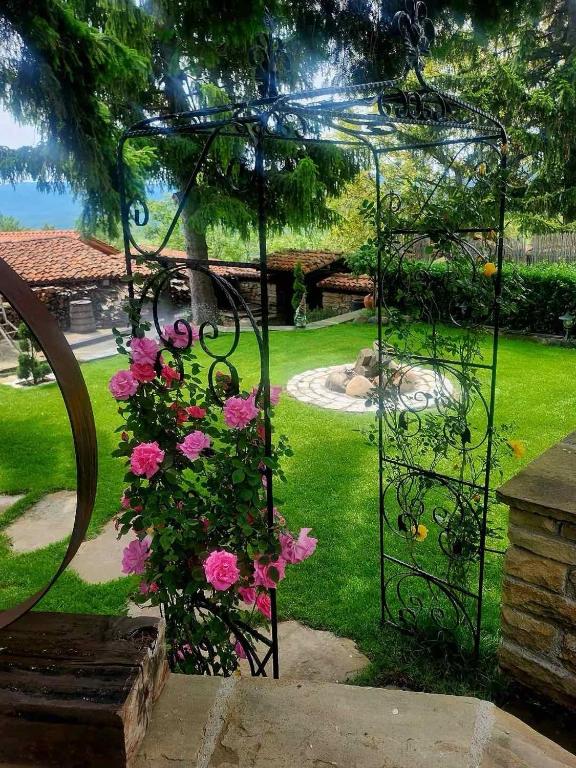 a garden with a metal structure with pink flowers at Разбойна in Zheravna