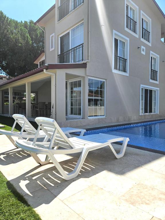 two white lounge chairs sitting next to a swimming pool at Luxury 5BR Villa w Pool & Beach Access Ayvalık in Ayvalık
