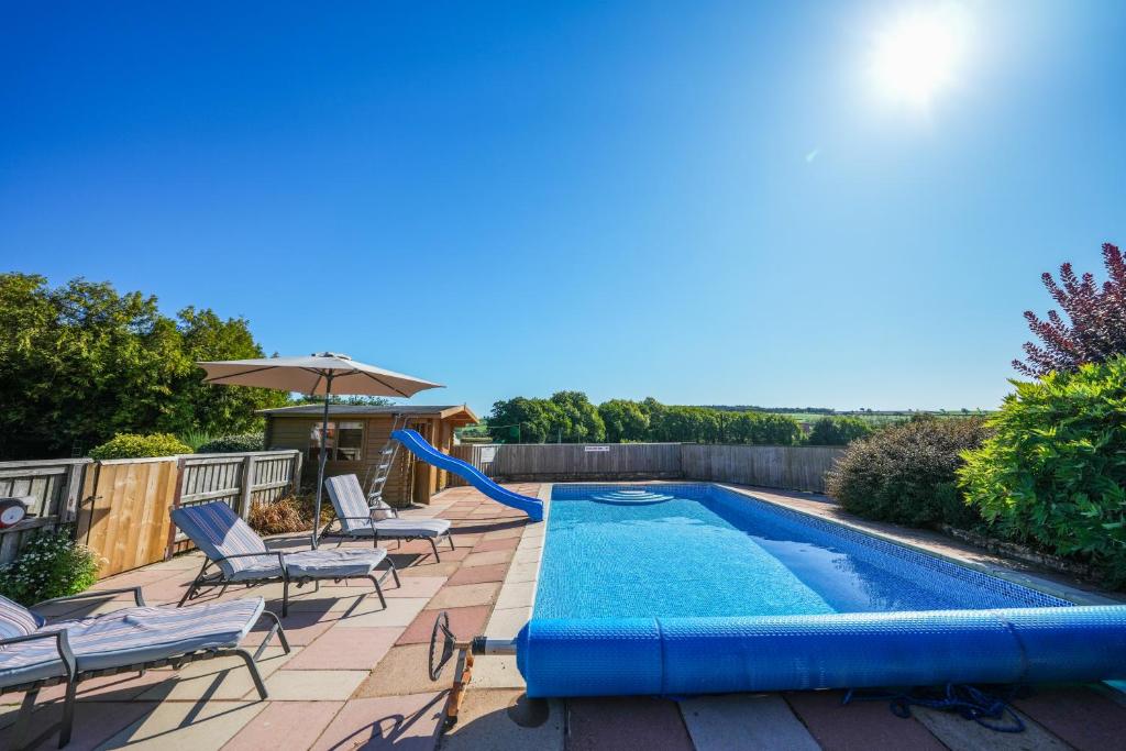 a pool with a slide next to chairs and an umbrella at Honeysuckle Cottage in Hele