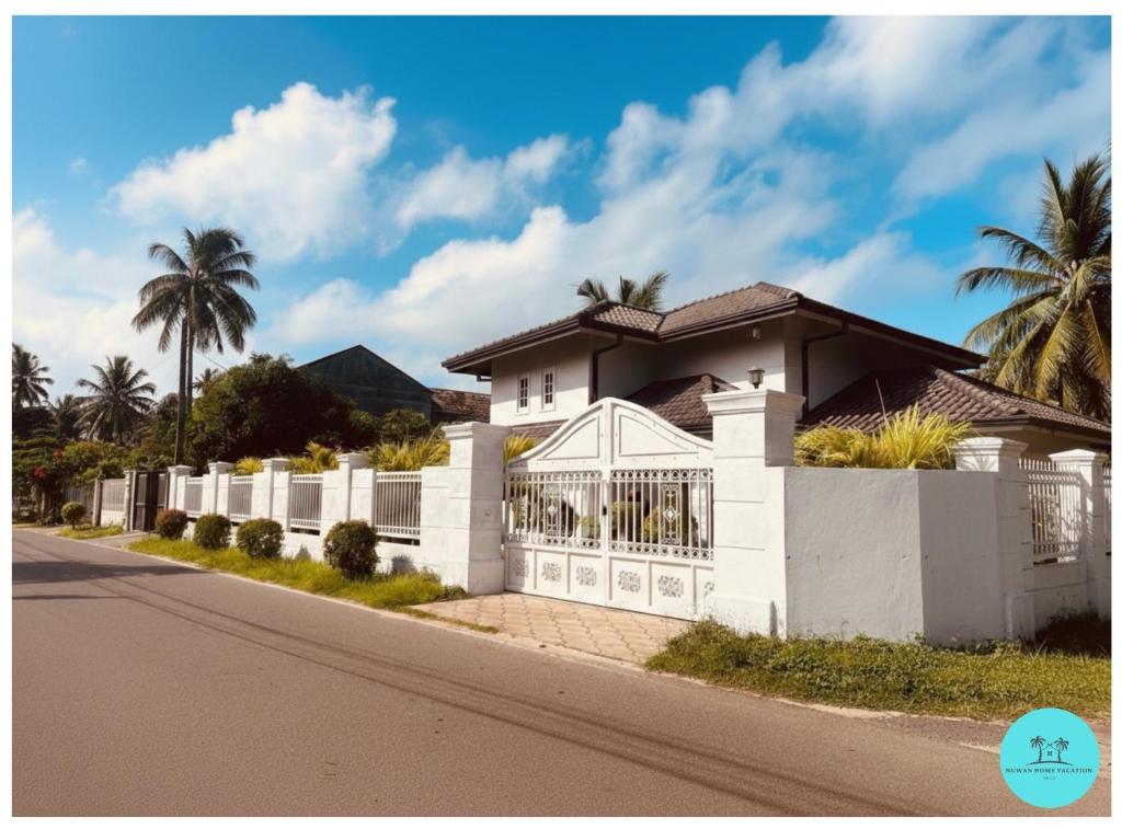 a white house with a fence and palm trees at Nuwan Home Vacation Villa in Wennappuwa