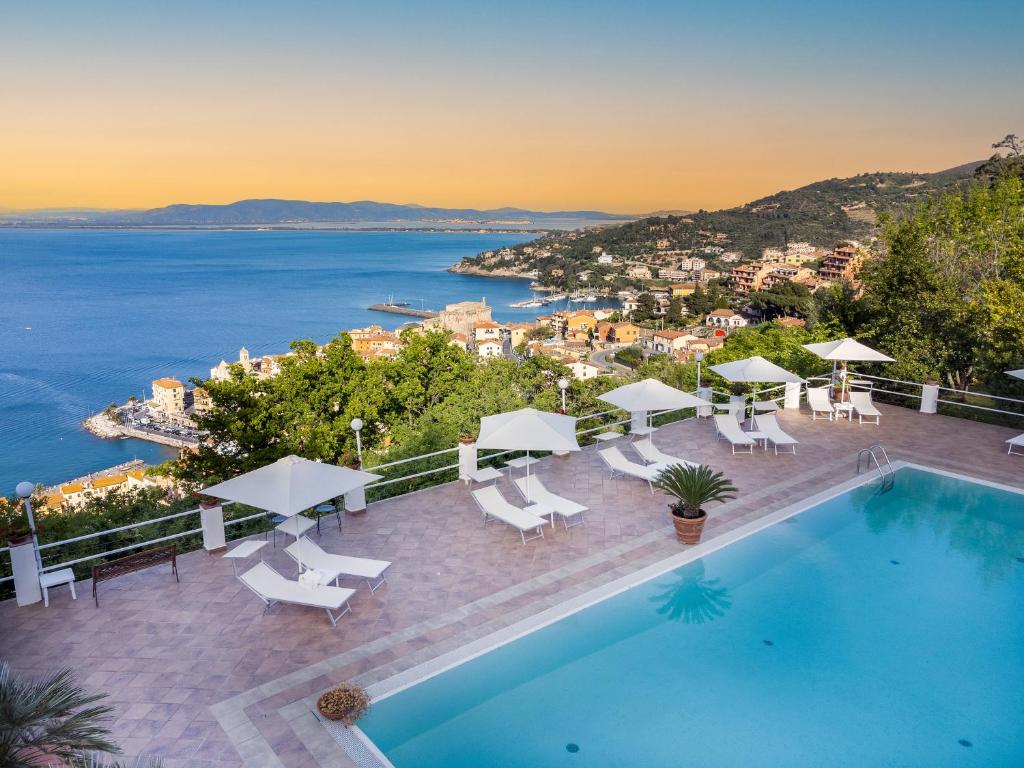 a pool with chairs and umbrellas and the ocean at Hotel Vittoria in Porto Santo Stefano