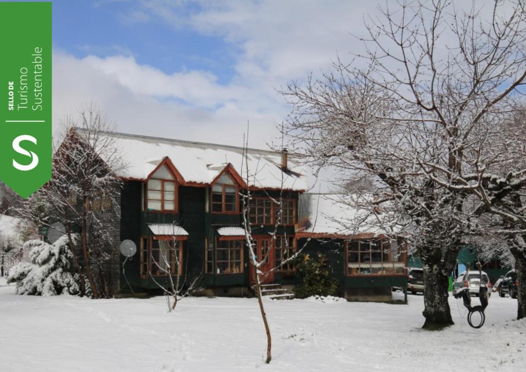 a house in the snow with a tree in front at CasaVerde Hostal Ecologico in Malalcahuello