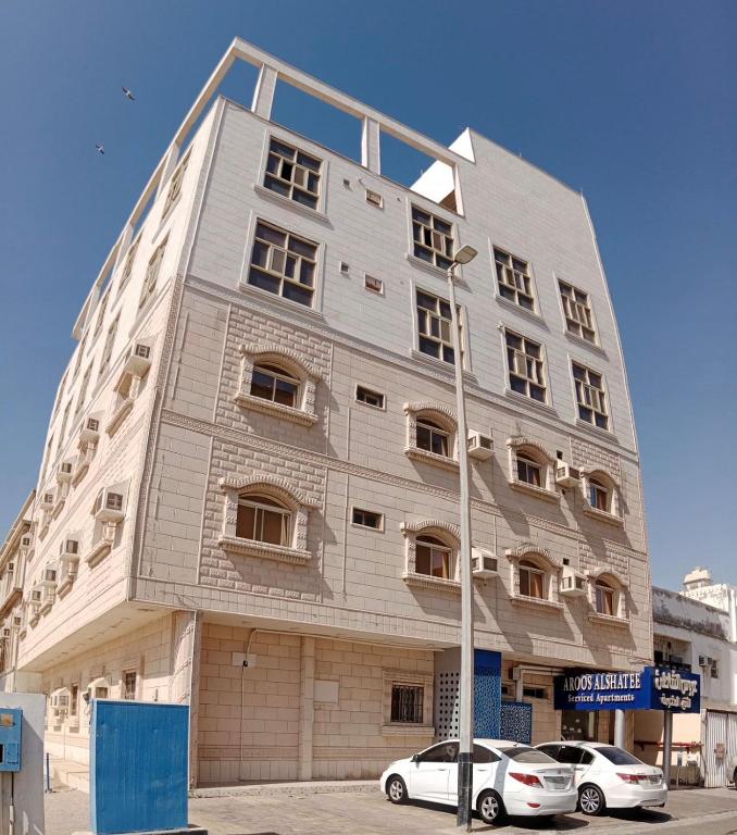 a large white building with cars parked in front of it at عروس الشاطئ للشقق المخدومة in Umm Lajj