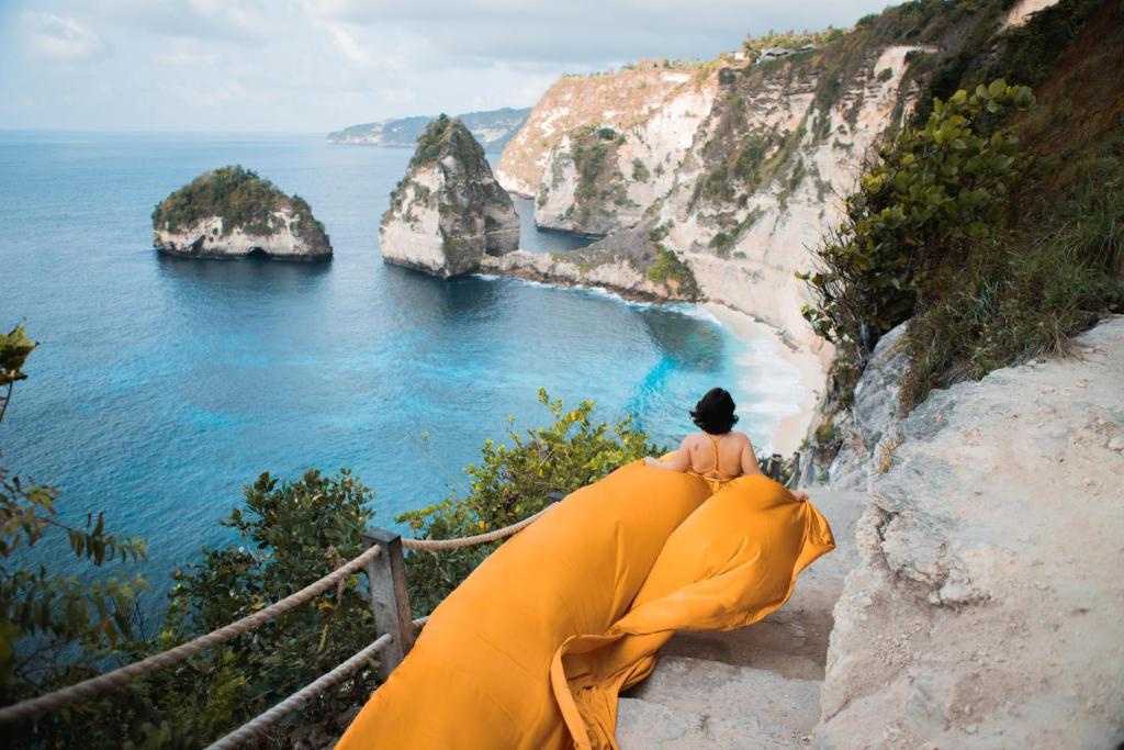 a woman sitting on a cliff looking at the ocean at Arthas Villa Nusa Penida in Polilit