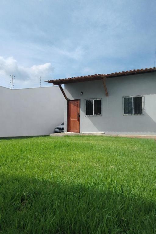 a white building with a door and a grass field at Casa, Perto de Praias, Shoppings e Valparaíso in Maioba